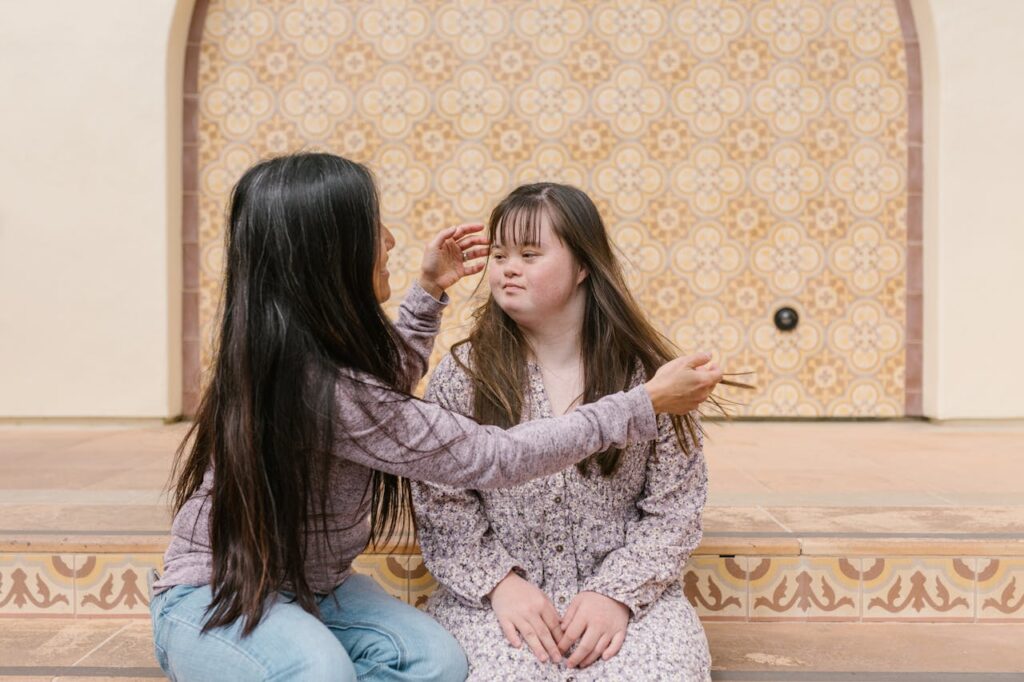 A mother lovingly adjusts her daughter's hair as they sit together on steps.